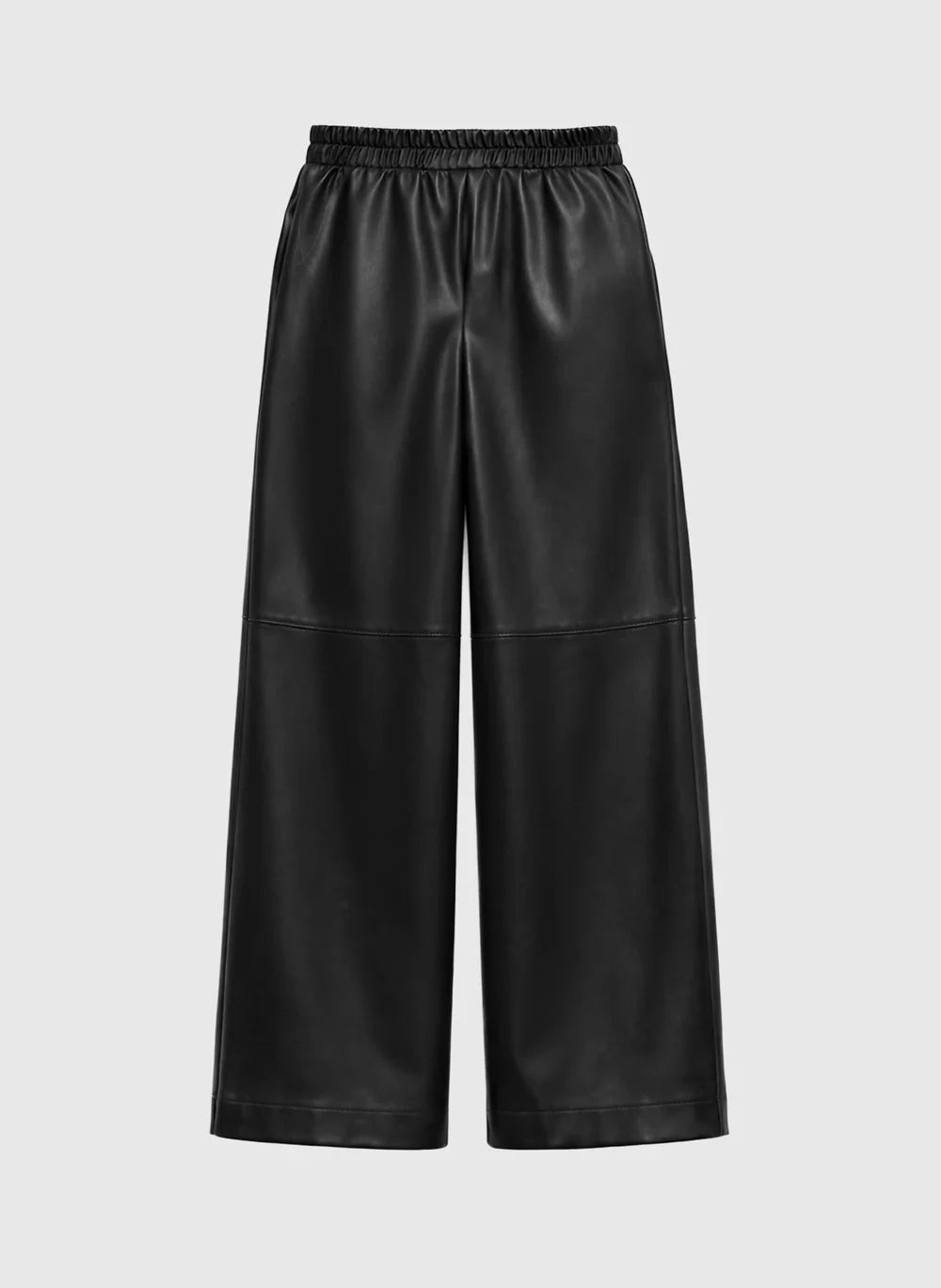 A woman models a black short-sleeve jumpsuit with ruffled detailing on the chest and wide-leg pants, standing in a bright, elegant room with wood floors and neutral walls.