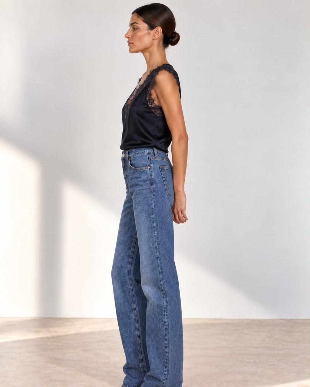 A woman modeling a dark navy satin top with black lace trim and blue straight-leg jeans against a light gray studio background.