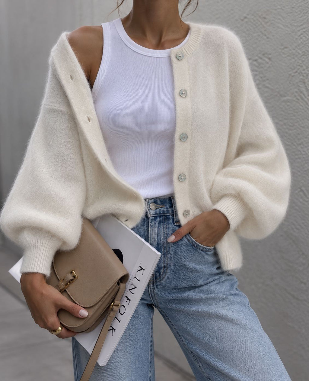 A close-up of a woman wearing a fuzzy cream-colored cardigan sweater with silver buttons, paired with blue jeans.